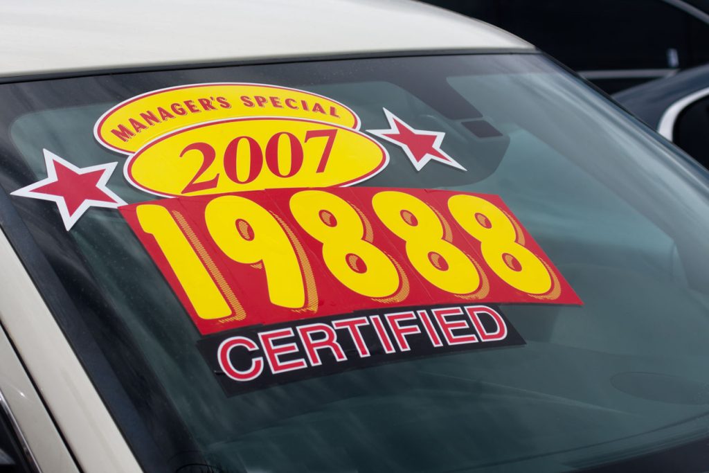 A used vehicle on a dealership lot displays a large windshield sticker advertising a manager's special price of $19,888 for a certified 2007 model. Prominent price stickers are commonly used to attract shoppers, but advertised prices must accurately represent what consumers can expect to pay, making pricing transparency an important consideration for both dealerships and used car buyers.